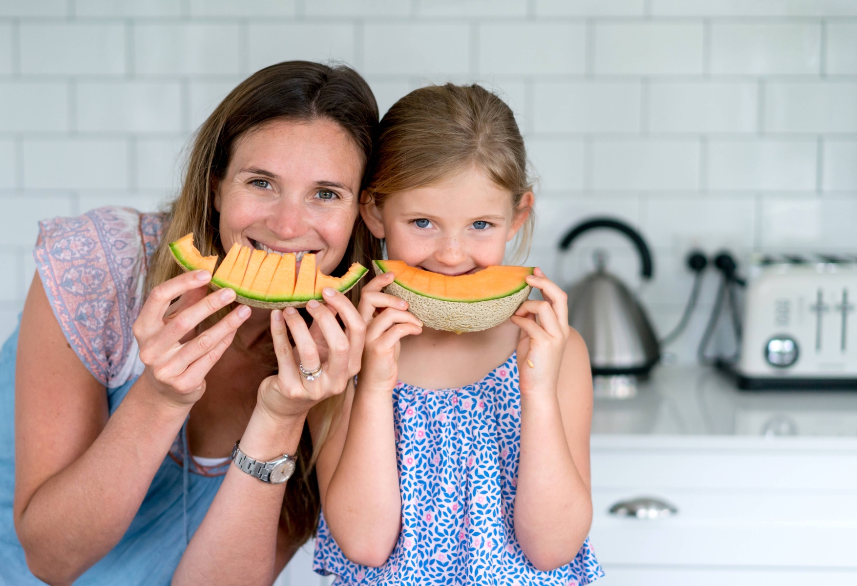 parent and child eating orange melon smiling in kitchen