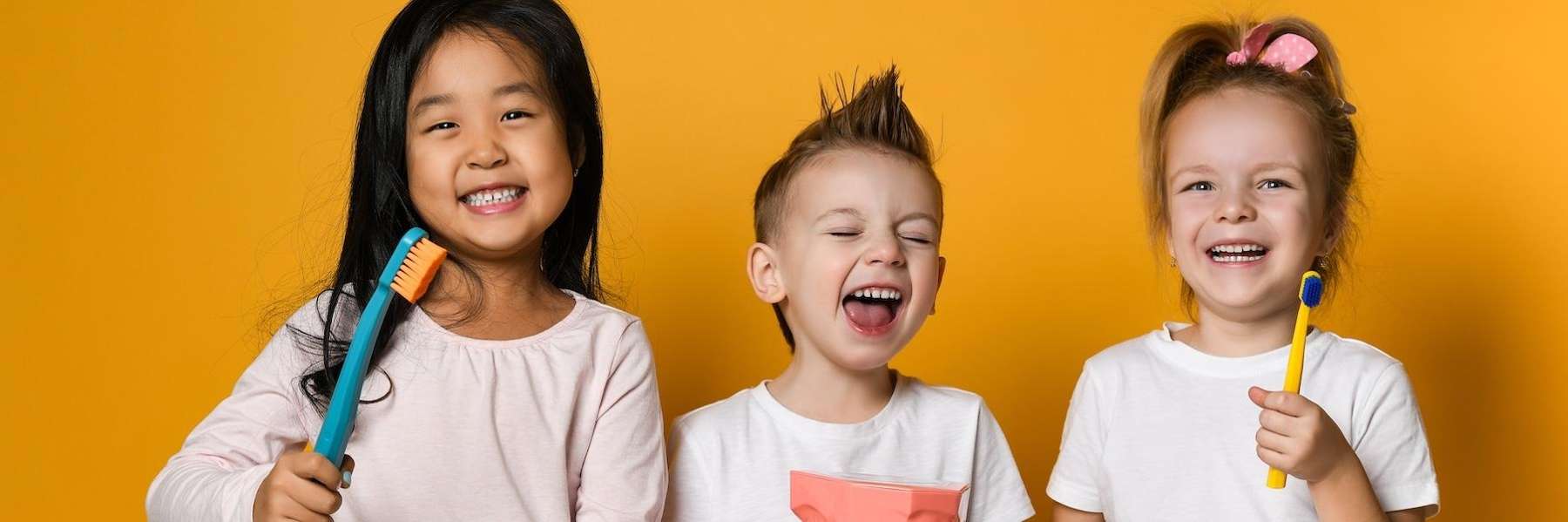 Three laughing children holding toothbrushes