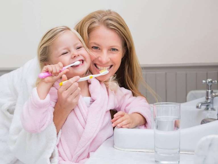 A mother and daughter brushing their teeth in their bathrobes