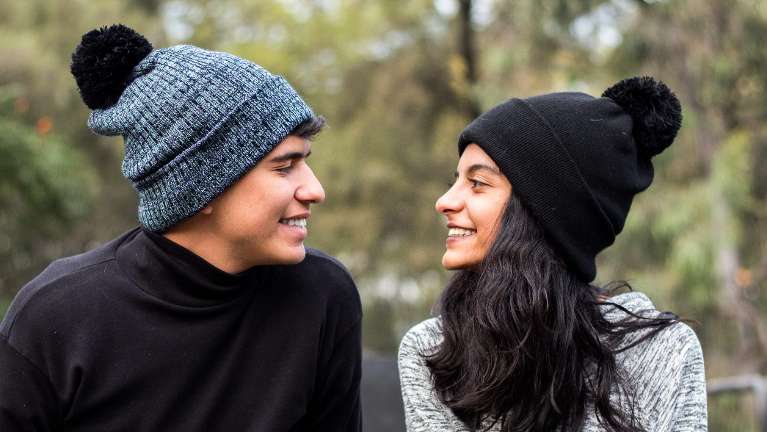2 People wearing beanies and smiling at each other