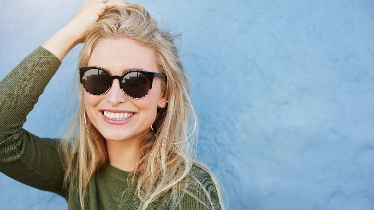 A smiling woman in sunglasses against a blue wall